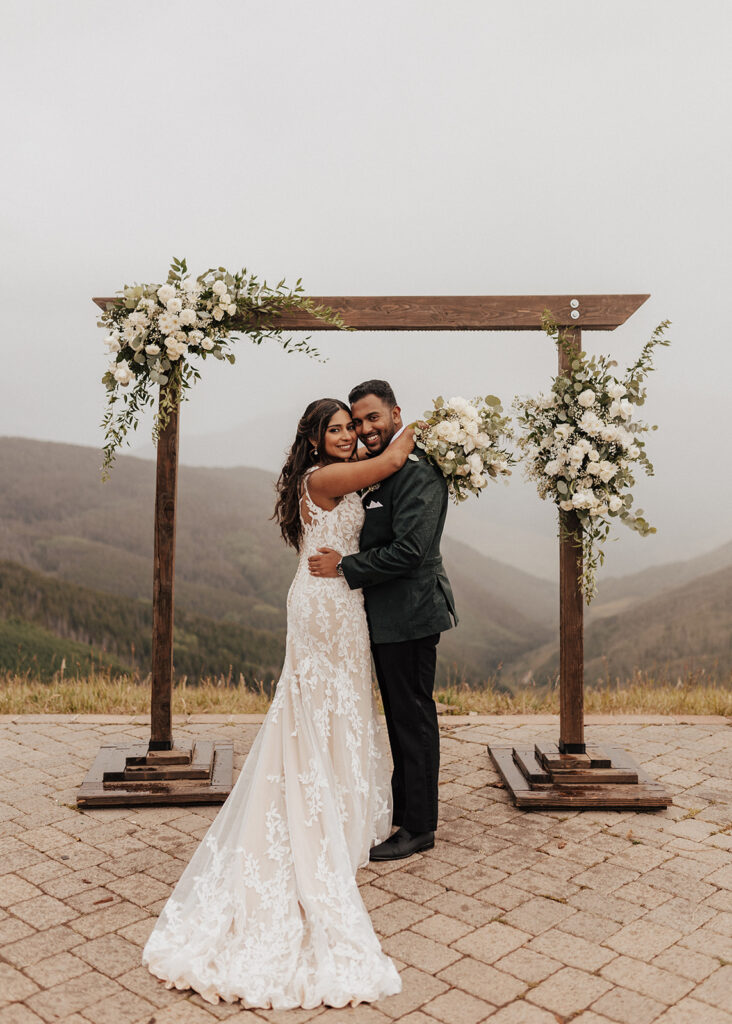 Bride and groom portrait under floral arch atop Vail Mountain, CO.