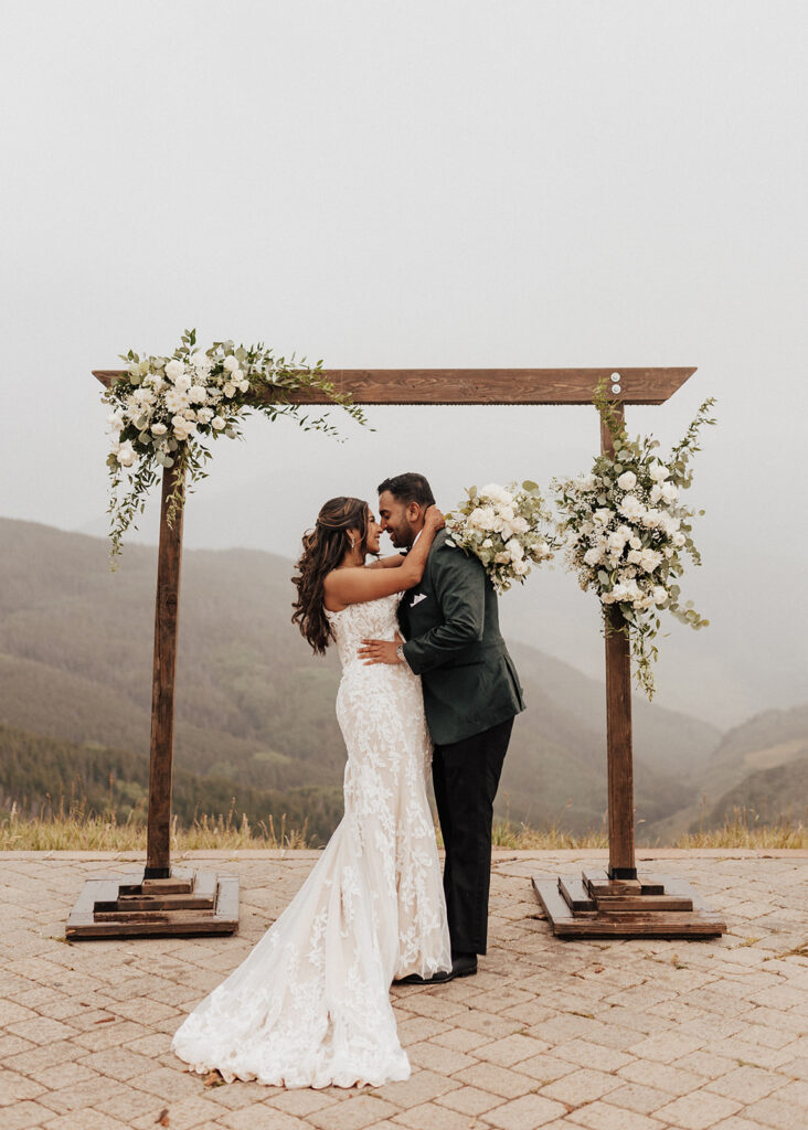 Bride and groom portrait under floral arch atop Vail Mountain, CO.