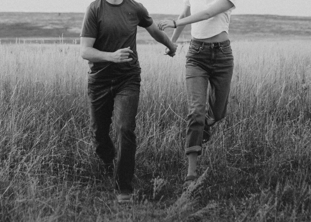 Engaged couple running in open field in Boulder, CO