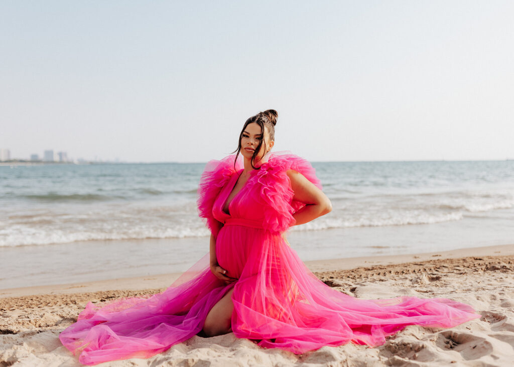 Pregnant woman sitting on the beach for maternity photos.