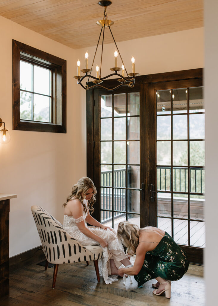 Bridesmaid helping bride fasten her shoes at Black Canyon Inn in Estes Park, CO